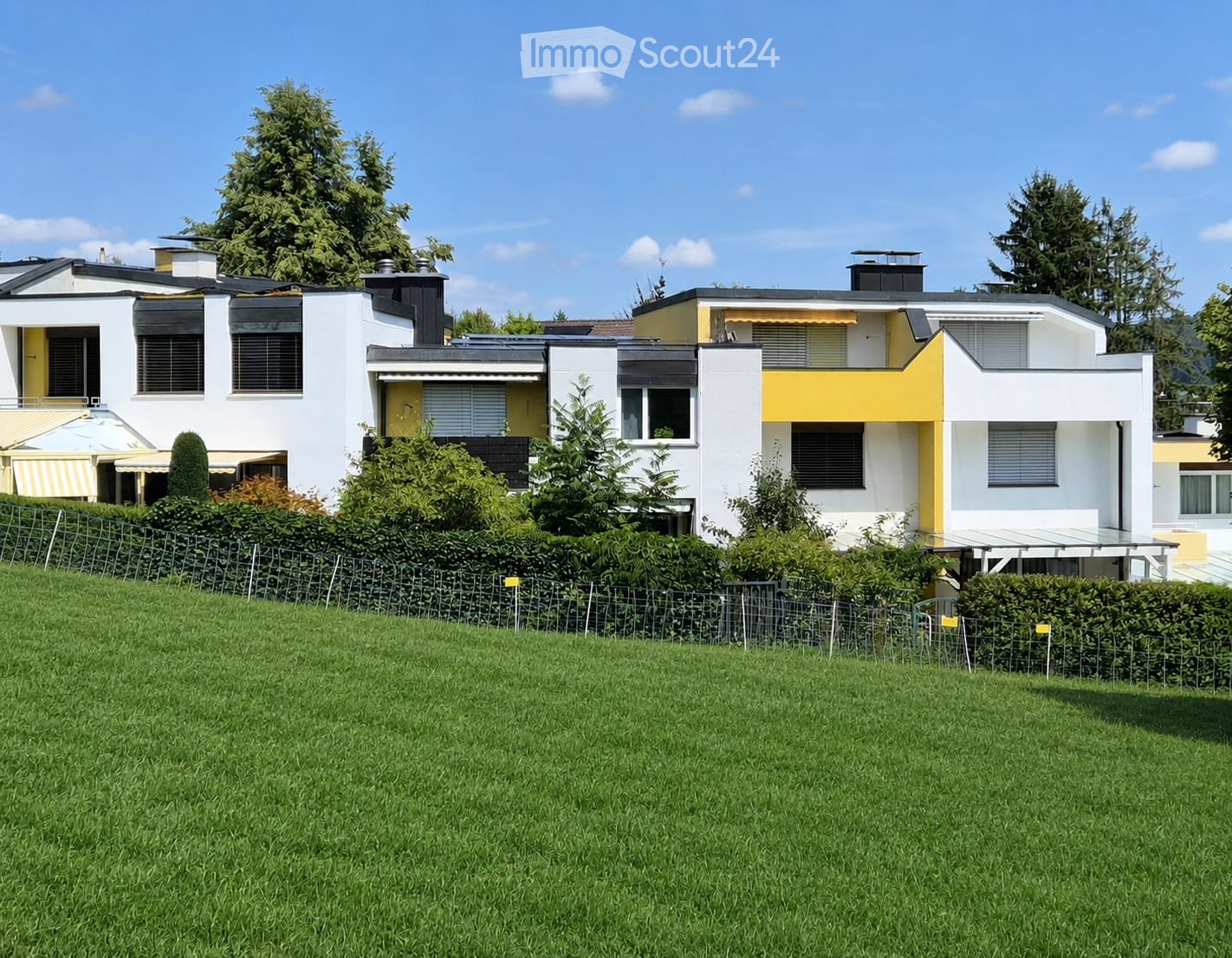 Modern two-story house with white and yellow exterior, multiple windows, and a well-maintained lawn in front.