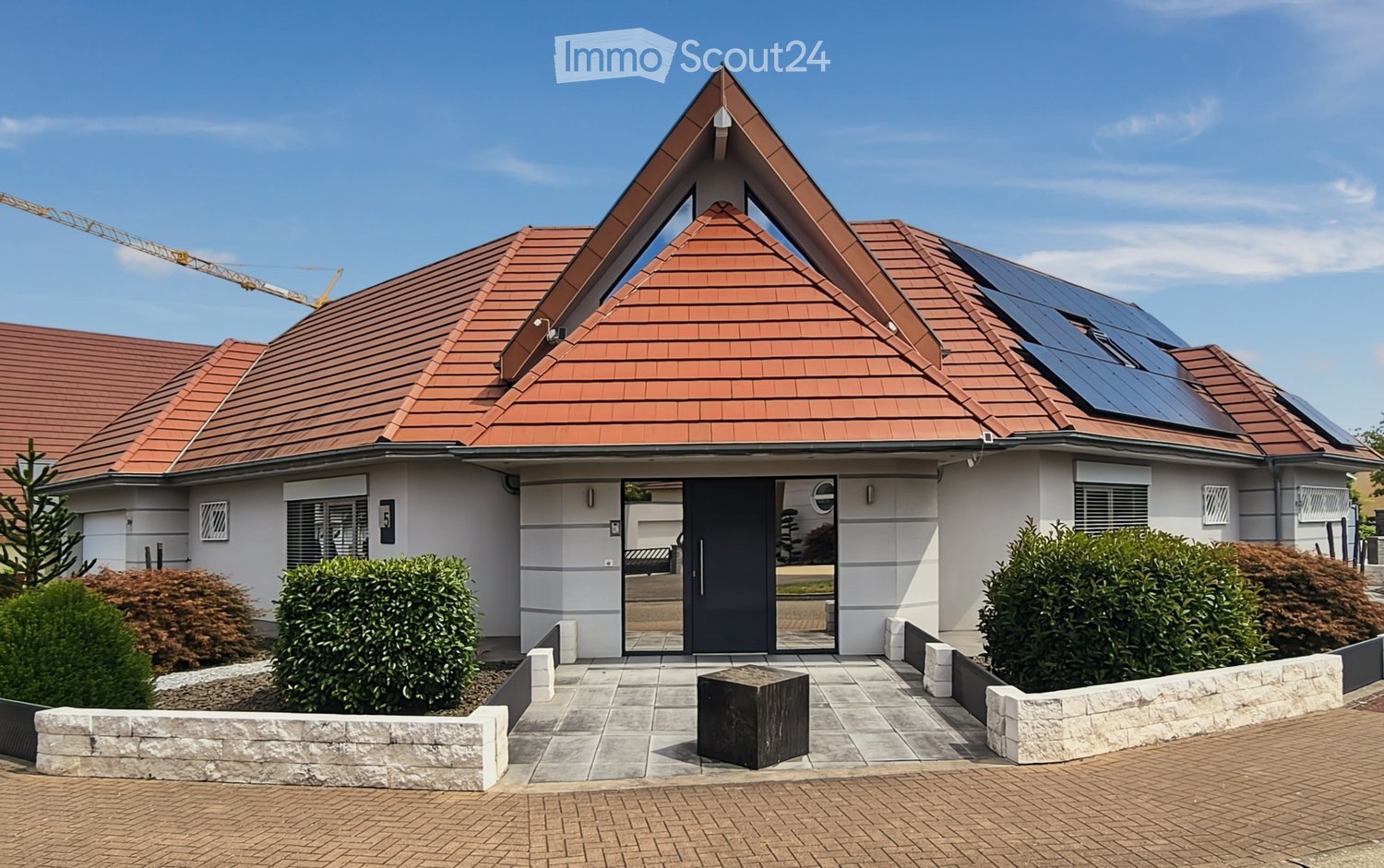 Modern two-story house with red tile roof, solar panels, white exterior, and landscaped front yard with shrubs and a stone pathway.