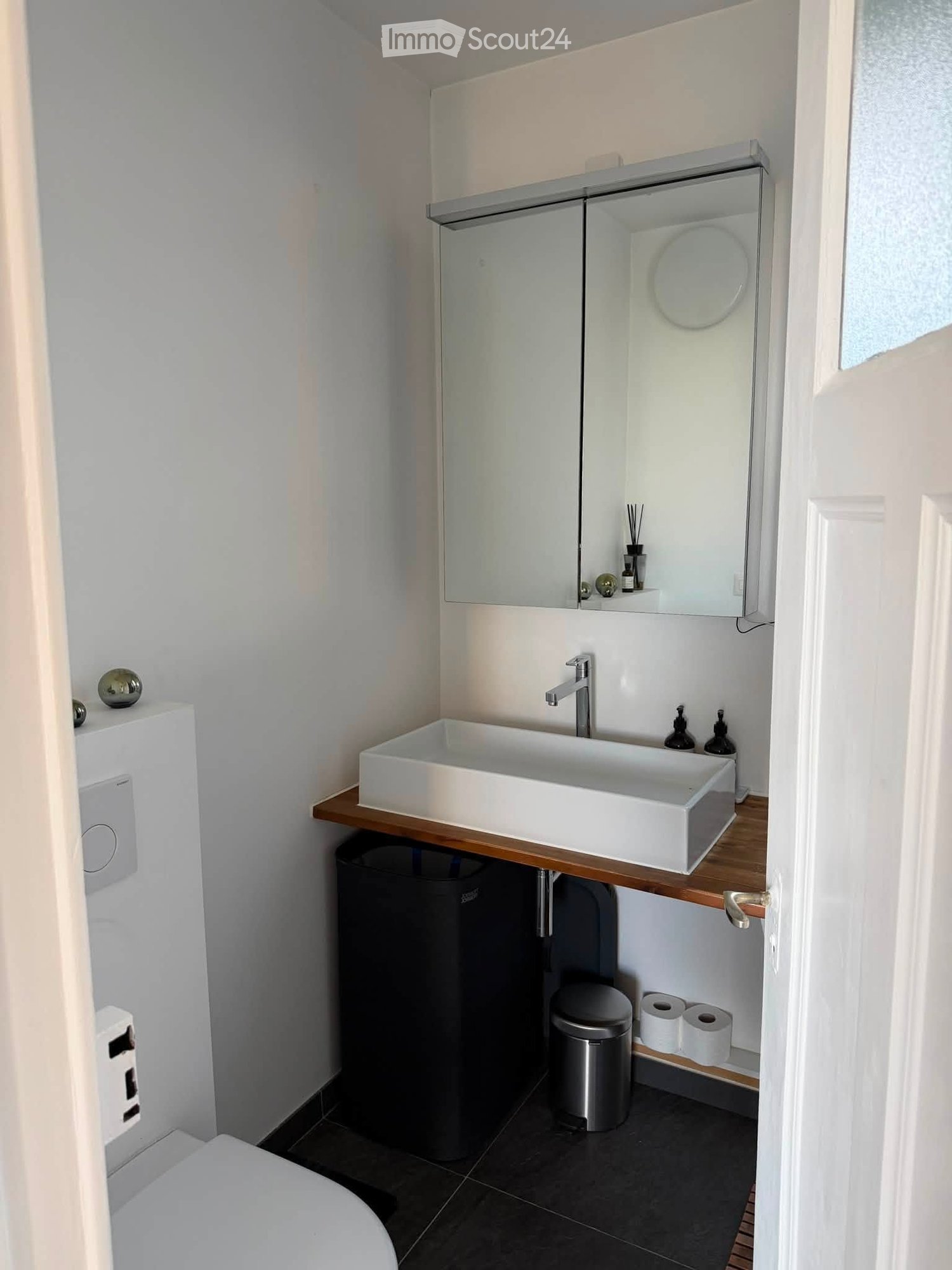 Modern bathroom with a white sink, chrome faucet, large mirror, toilet, and dark tiled floor.