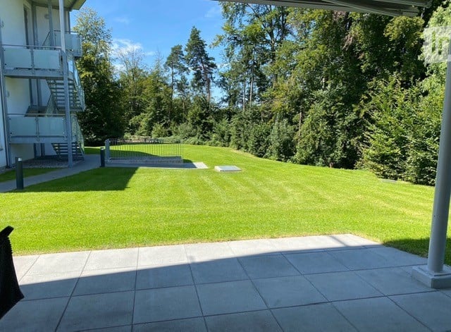 lawn with trees and shrubs, stairs leading to building, paved walkway, garden with bench