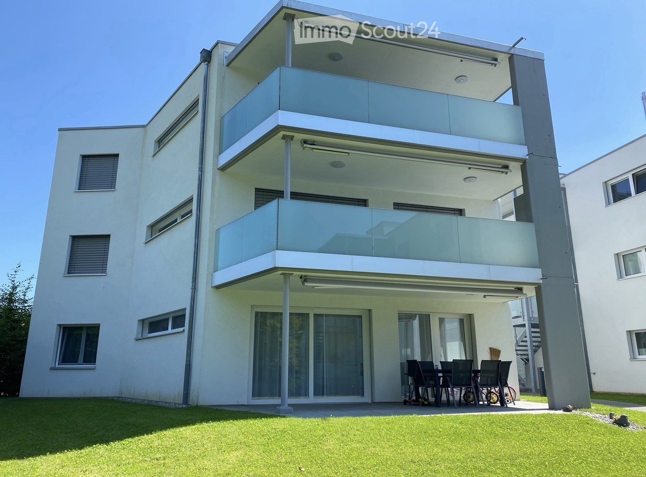 modern white building, 3 stories, multiple balconies, glass windows, outdoor dining area