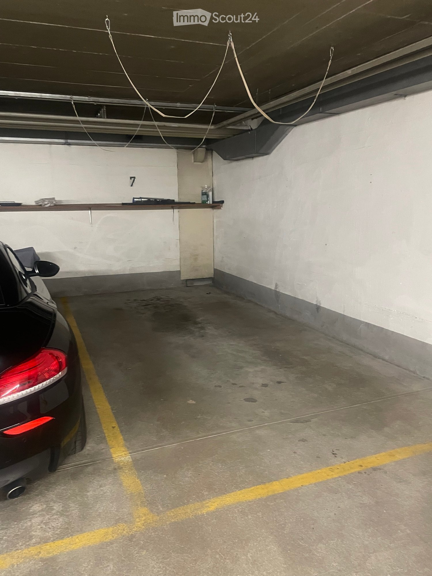 Underground parking space with concrete floor, white walls, yellow parking lines, and a parked car visible on the left side.
