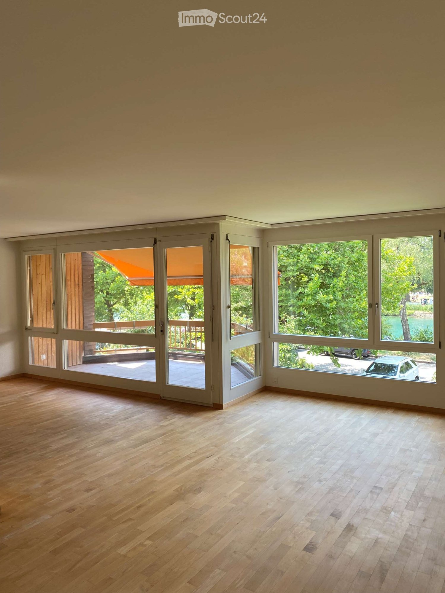 Empty room with wooden flooring and large windows and sliding doors leading to an outdoor area.