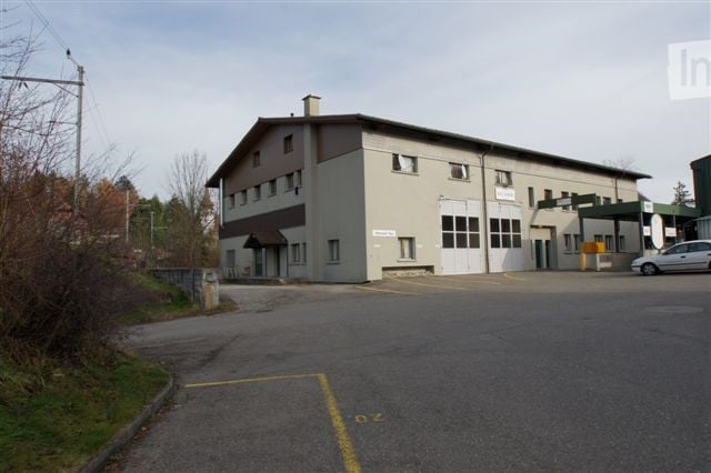 Industrial-style building with a large garage door, multiple windows, and a paved parking area.