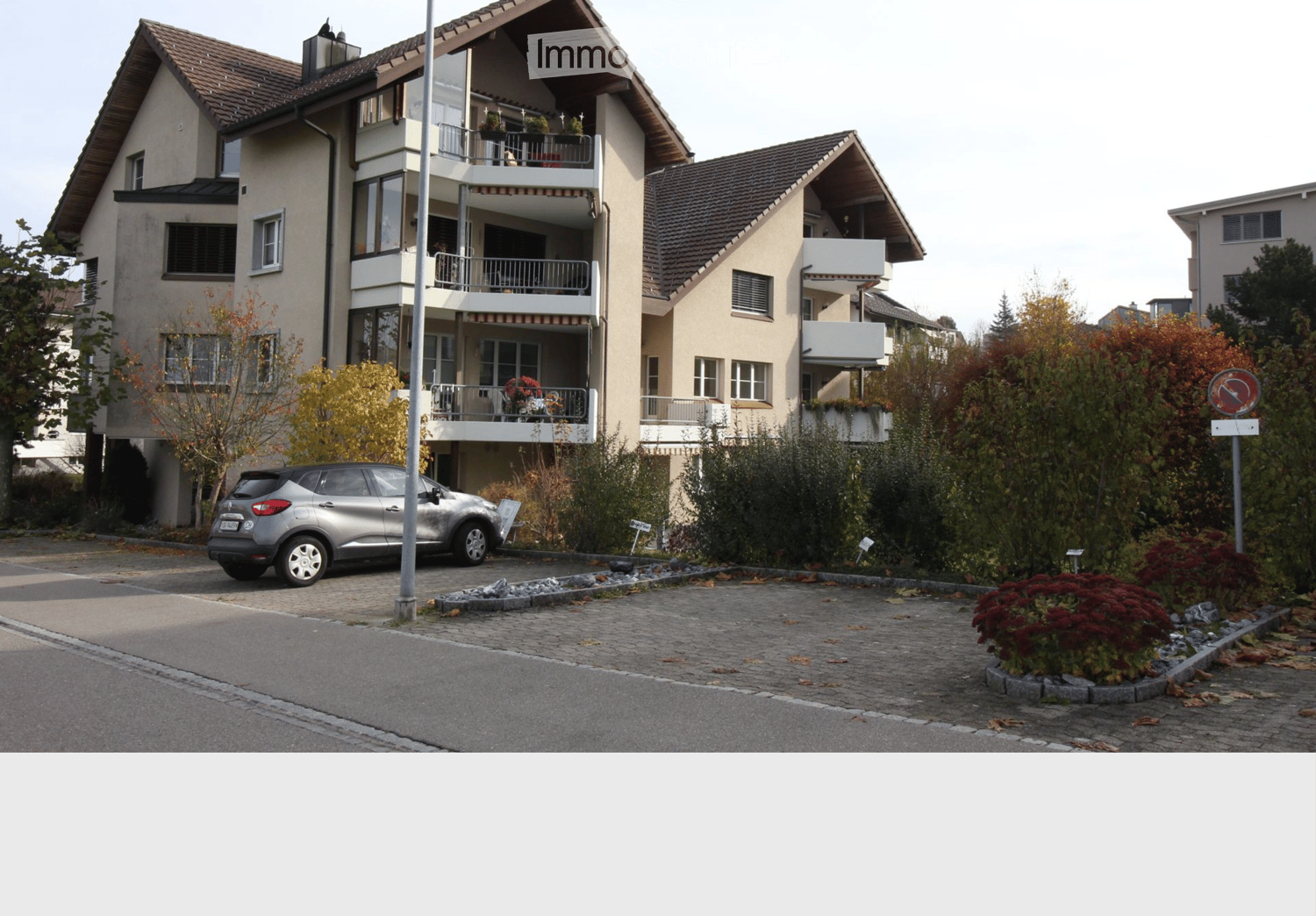 Two-story house with beige walls, multiple windows, balconies, and a parked car in front.
