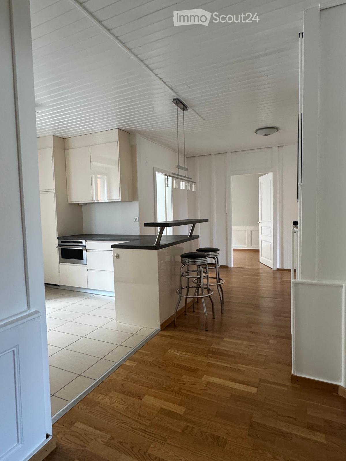 Modern kitchen with white cabinets, a black countertop, and a kitchen island with stools. The space features wooden flooring and pendant lighting.