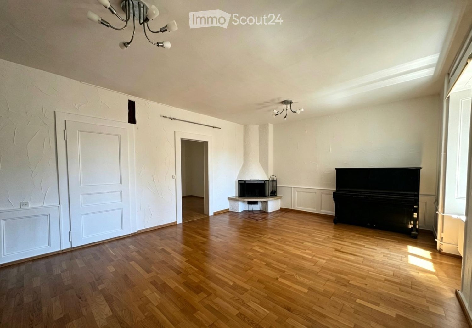 Spacious room with wooden flooring, a grand piano, a fireplace, and large windows allowing natural light.