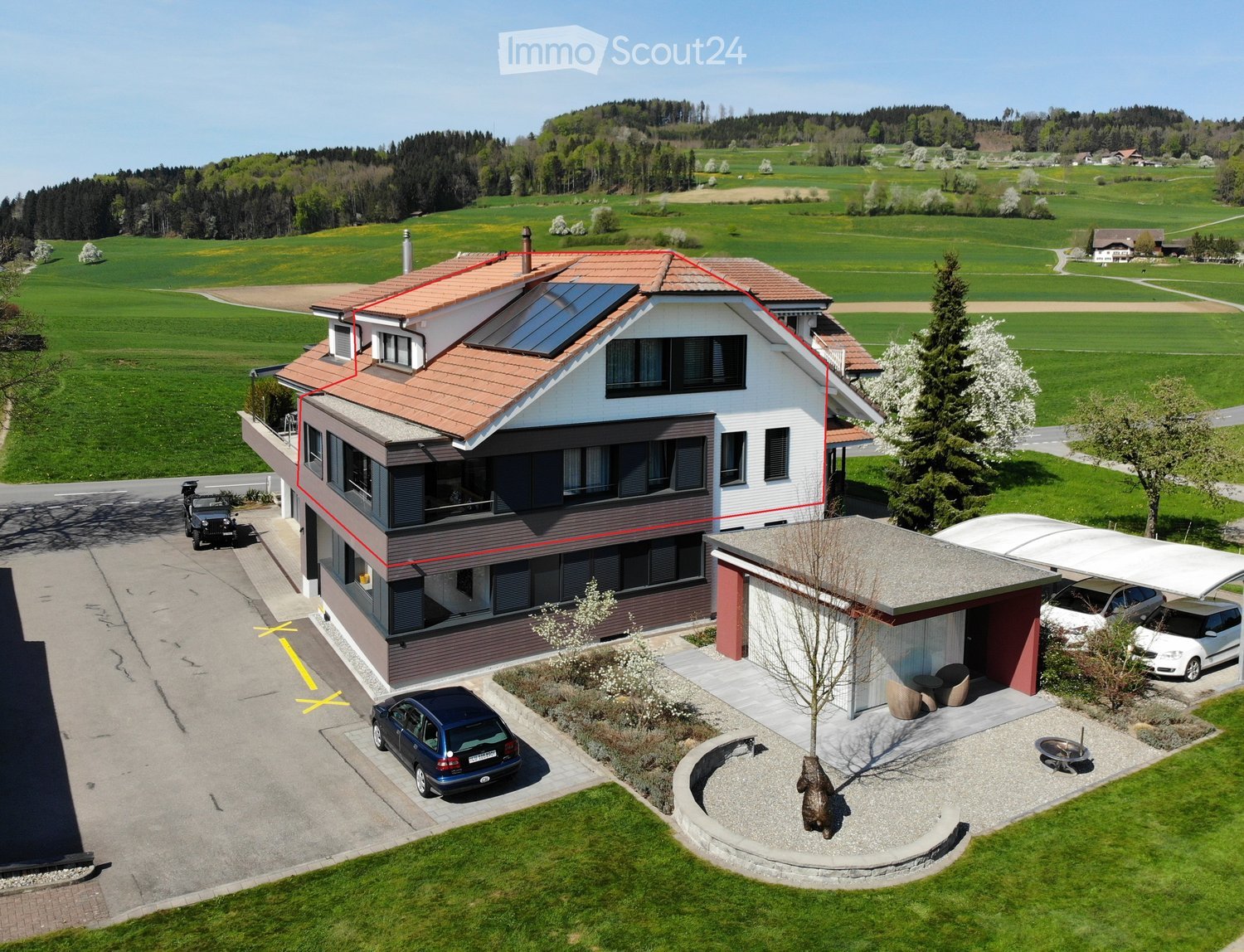 Two-story house with solar panels on the roof, surrounded by a well-maintained garden and driveway with parked cars.