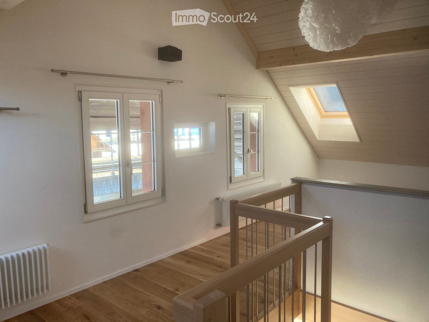 Bright hallway with wooden flooring, white walls, multiple windows including a skylight, and a wooden staircase railing.
