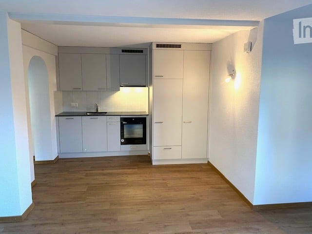 Modern kitchen with light grey cabinets, a sink, and an oven, featuring wooden flooring and white walls.