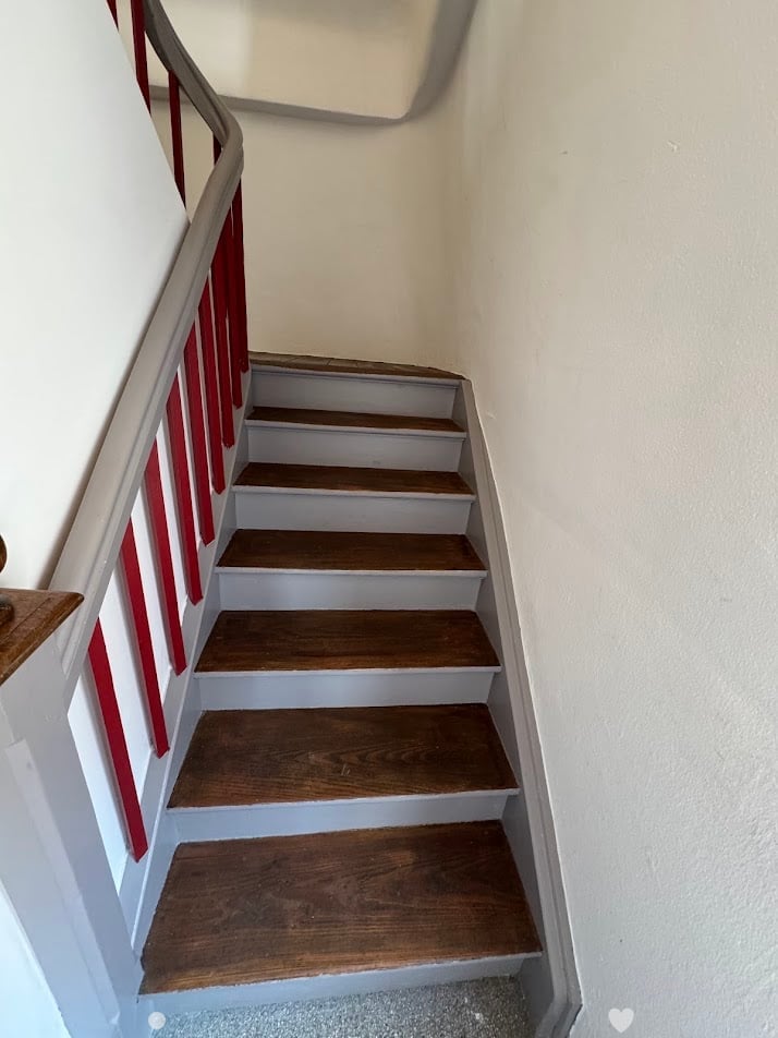 Wooden staircase with red handrail and white walls.