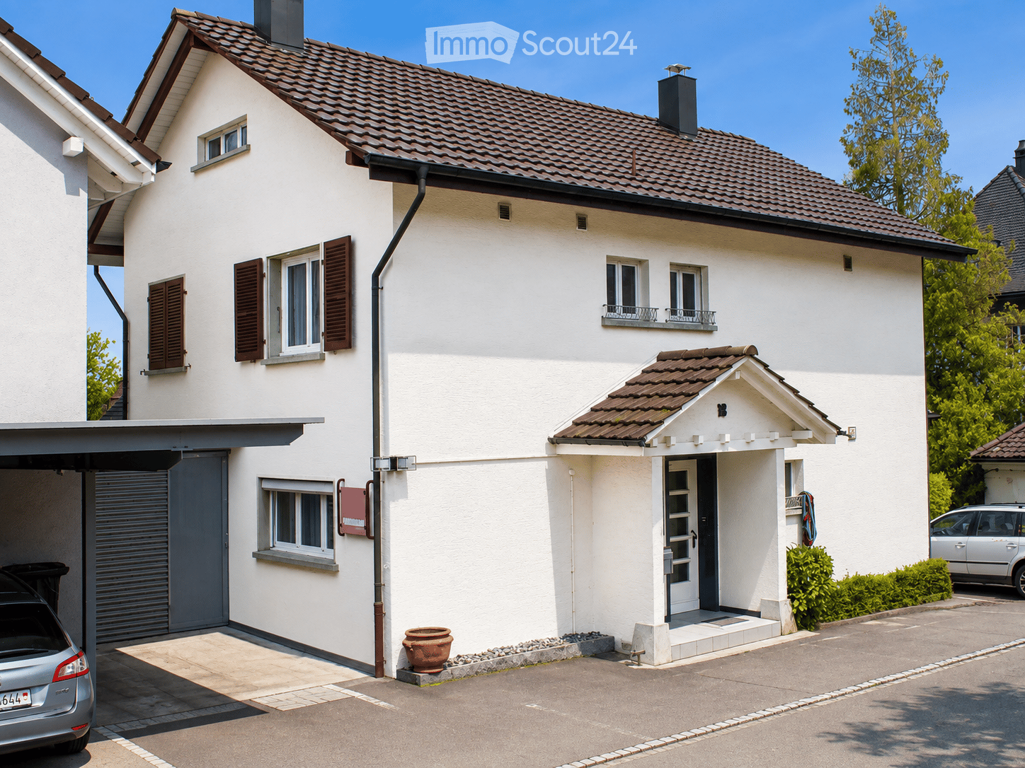 Two-story white house with a tiled roof, multiple windows with shutters, a garage, and a small entrance porch.