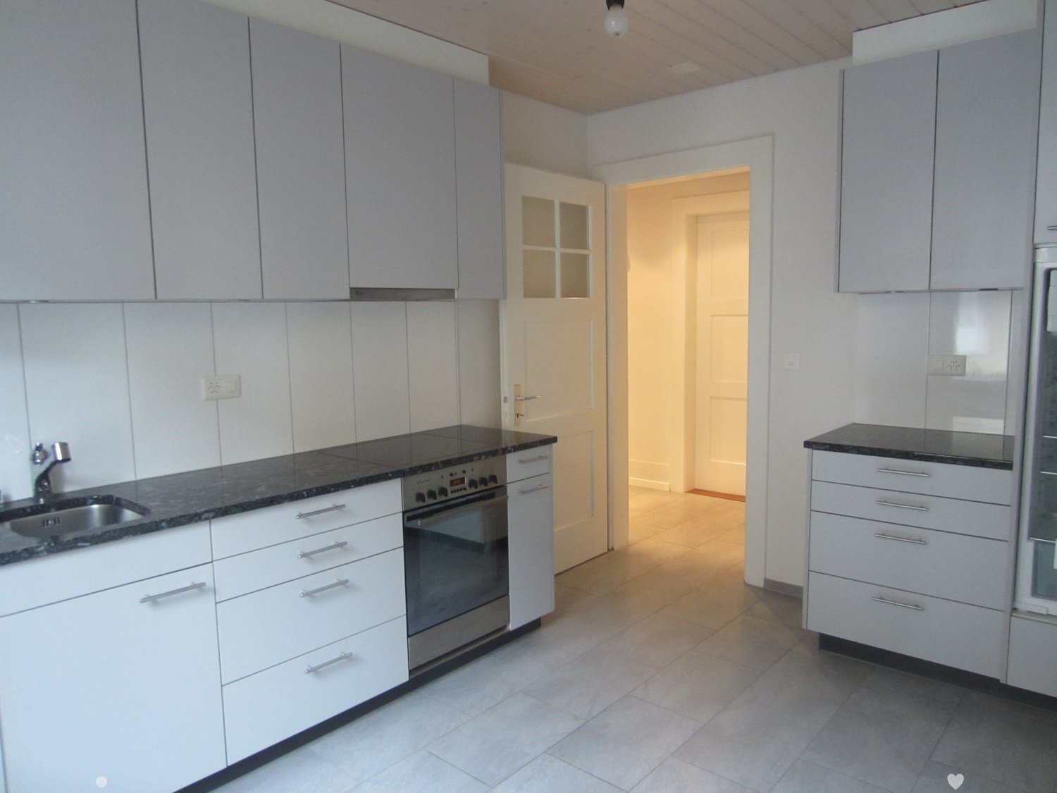 Modern kitchen with white cabinets, black granite countertops, stainless steel sink and oven, and a doorway leading to another room.