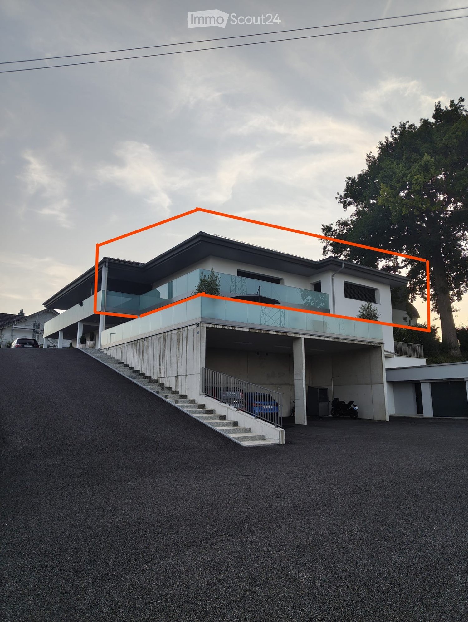 Modern two-story house with a raised ground floor, garage, and balcony on the upper level.