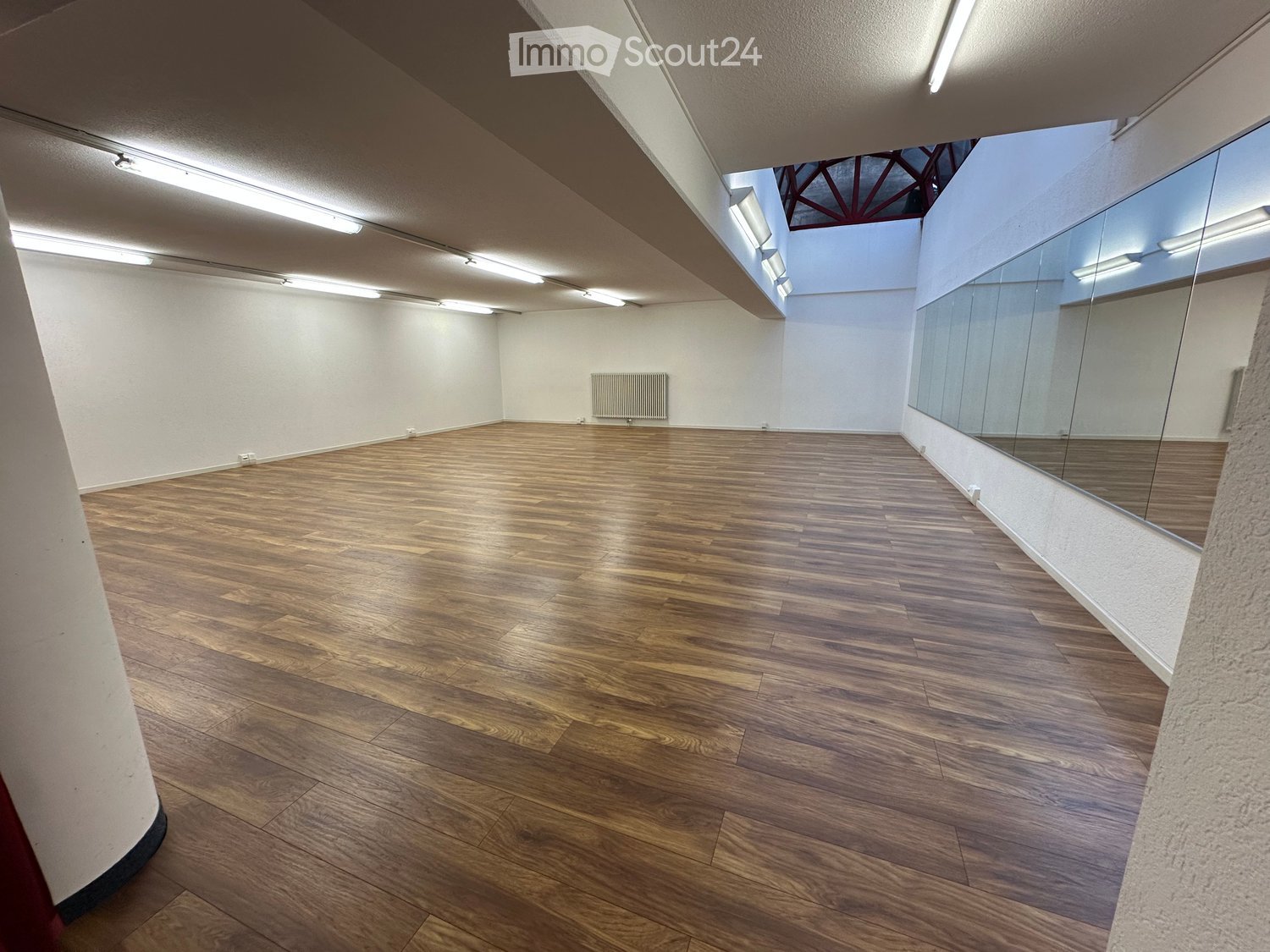 Empty room with wooden flooring, white walls, large mirrors, and a radiator. No furniture or equipment present.