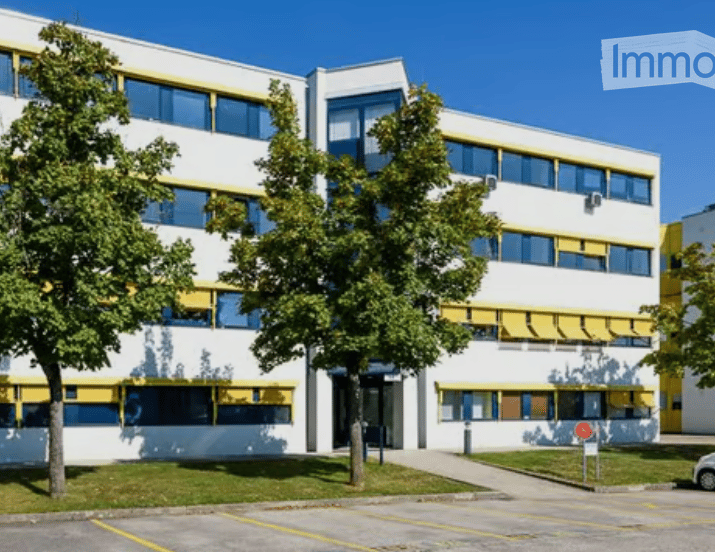 Modern multi-story building with white and yellow facade, large windows, and trees in front.