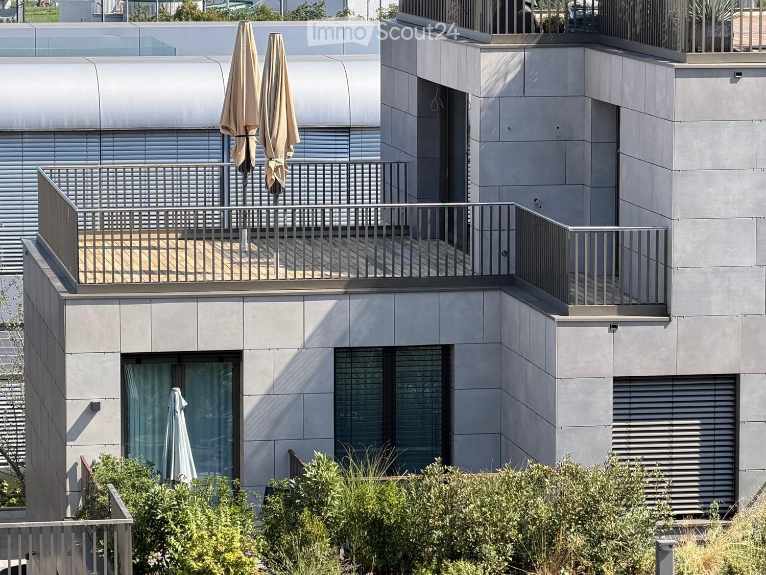 Modern building with grey facade, large windows, and balconies featuring metal railings and closed umbrellas.