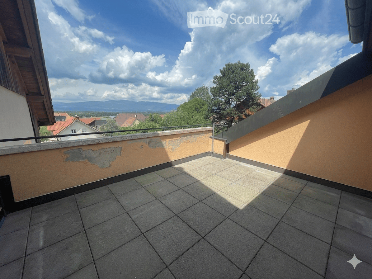 Balcony with tiled floor, low wall, and railing, overlooking a landscape with trees and distant mountains.