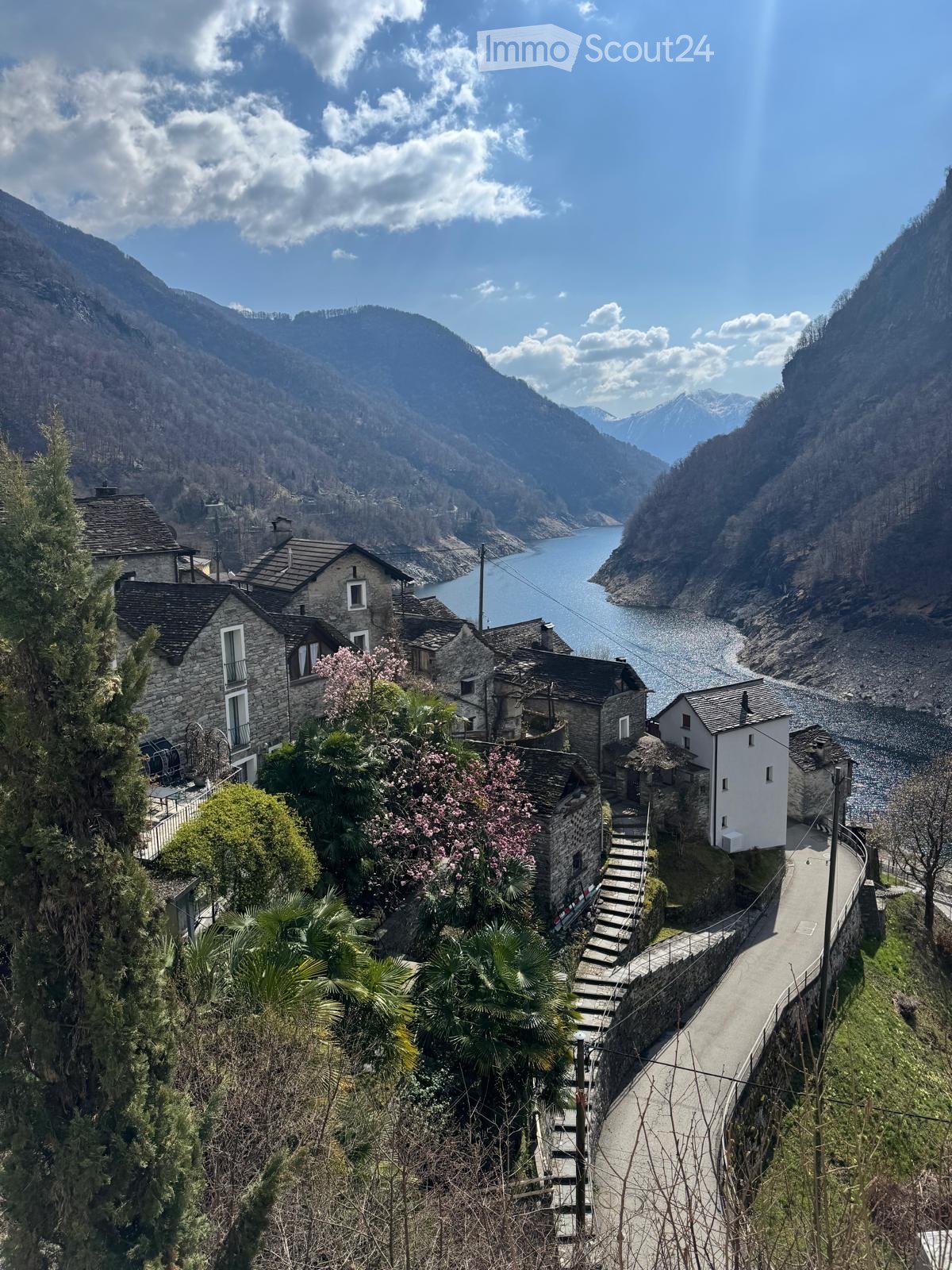 A picturesque village nestled in a mountainous valley, featuring stone houses, a winding road, and a serene lake in the background.