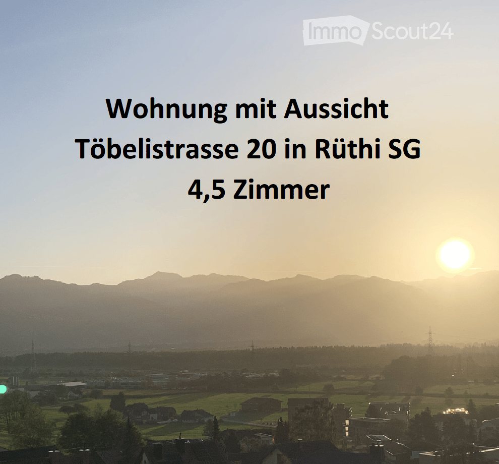 Panoramic view of a town with houses, fields, and distant mountains at sunset.
