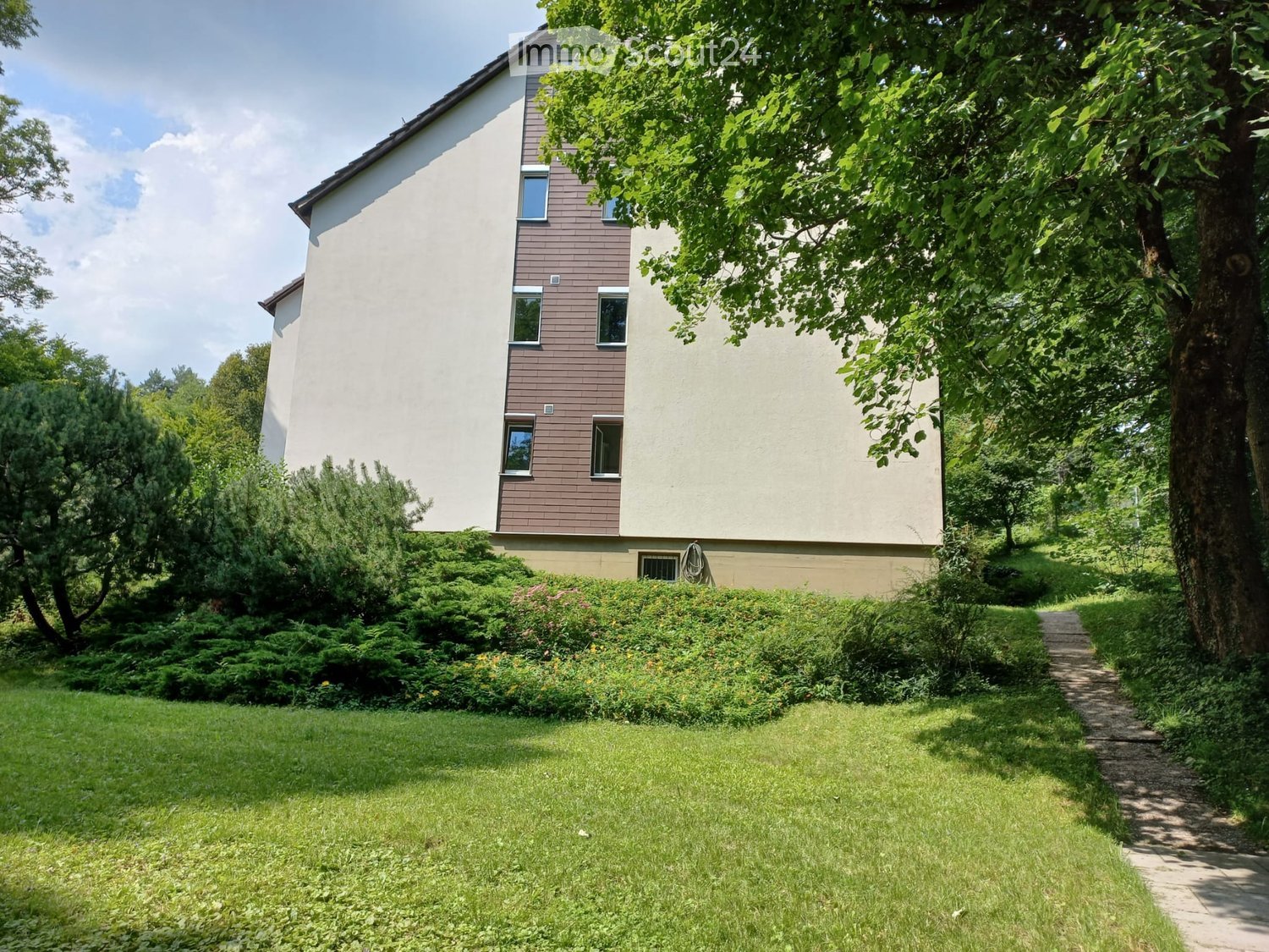 Two-story house with a combination of white and brown siding, multiple windows, and a well-maintained garden with a pathway leading to the entrance.