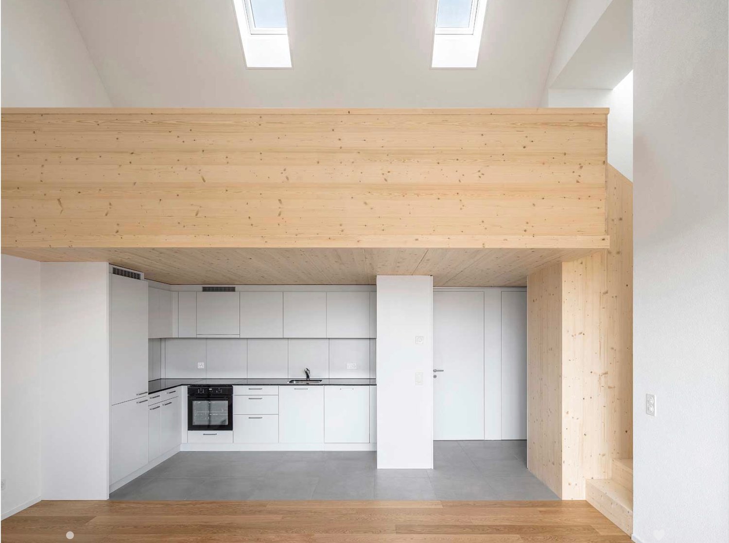Modern kitchen with white cabinets, stainless steel oven, and sink, featuring a raised wooden platform and skylight windows.