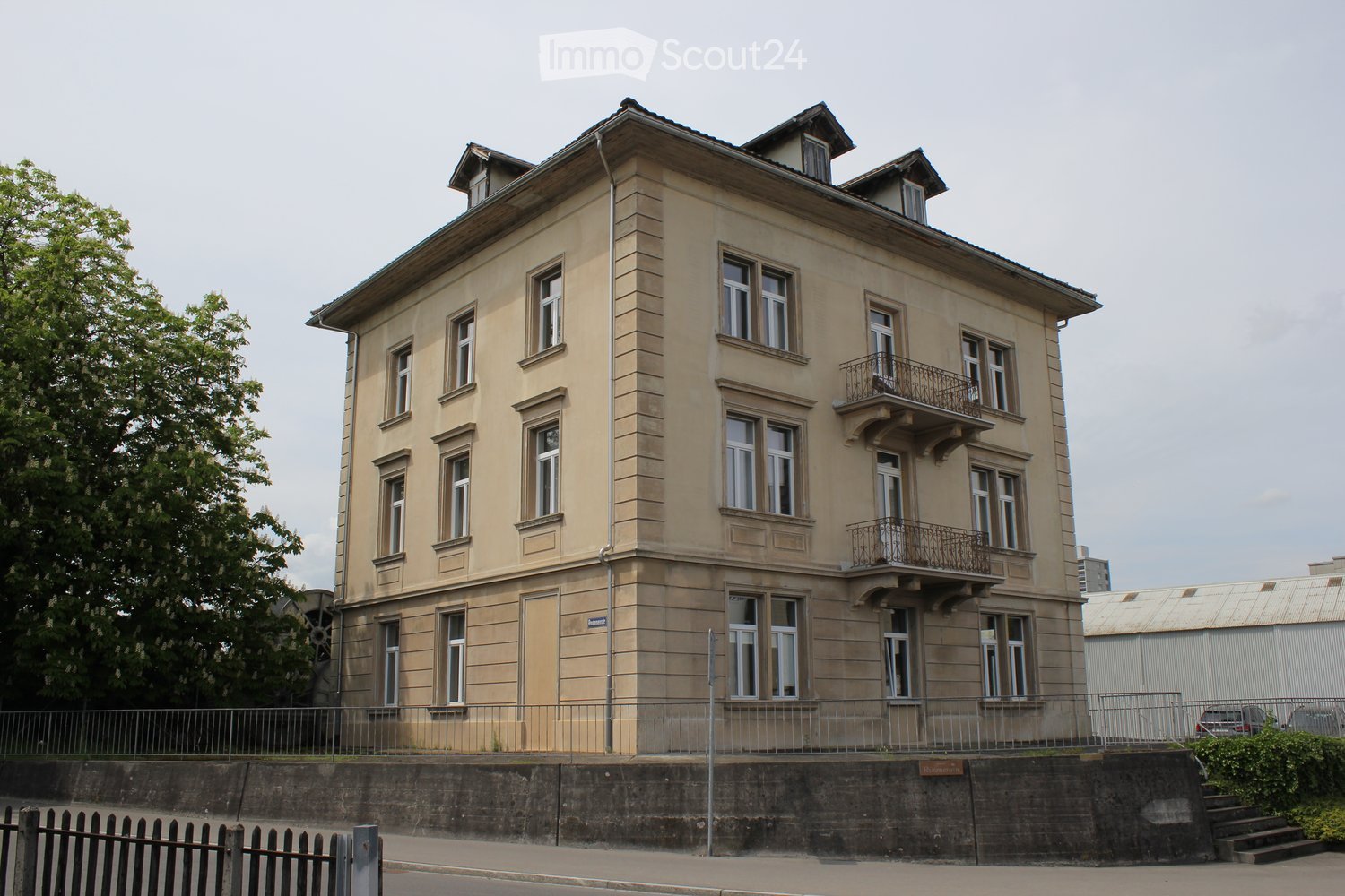 A multi-story residential building with beige facade, multiple windows, and a balcony on the upper floor.