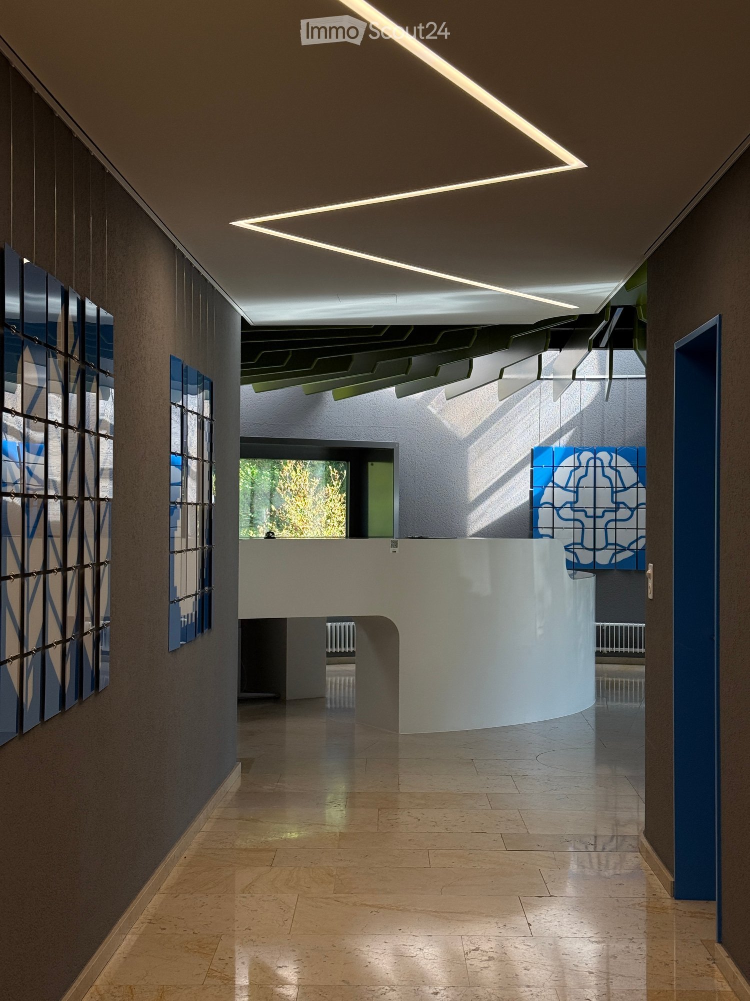 Modern hallway with sleek design, large windows, and geometric wall art. Features a curved white partition and recessed lighting.