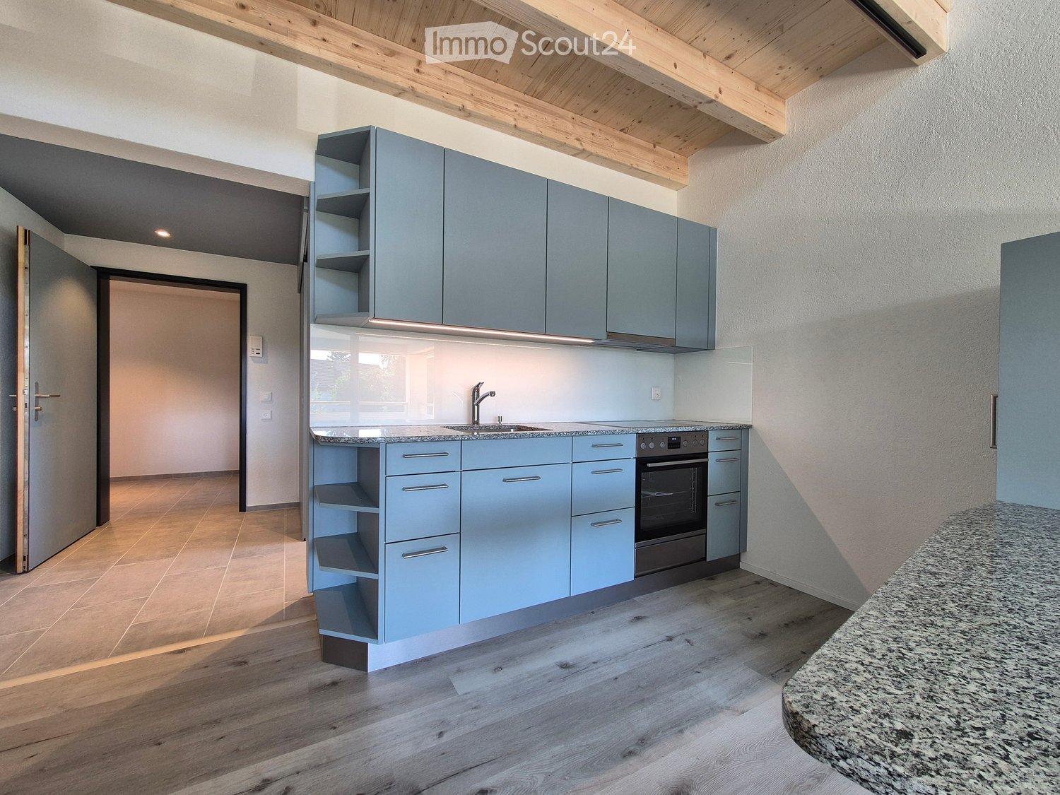 Modern kitchen with light blue cabinets, granite countertop, wooden flooring, and stainless steel appliances.