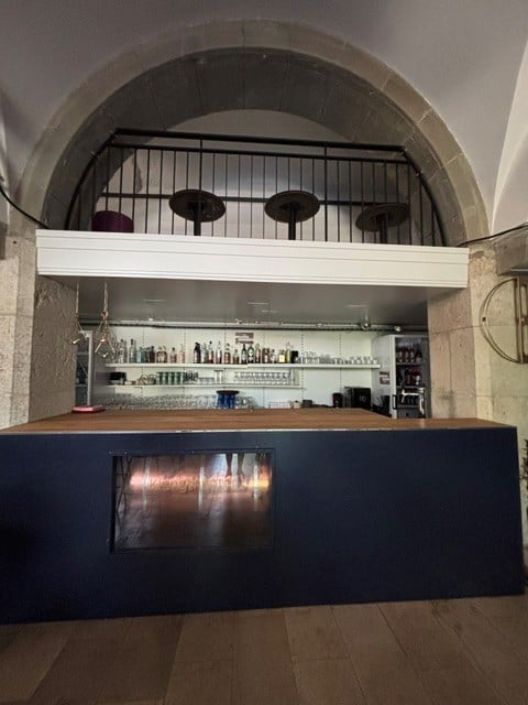 Modern bar area with dark blue counter, built-in shelves holding bottles and glasses, and a small fireplace embedded in the counter.