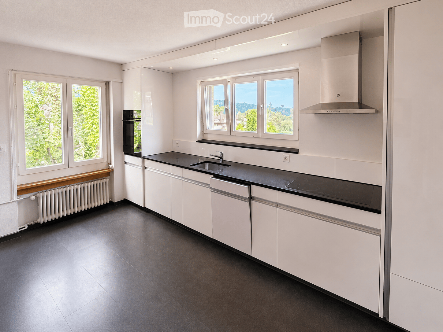 Modern kitchen with white cabinets, black countertops, stainless steel appliances, and large windows offering a scenic view.
