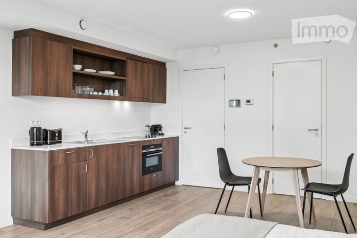 Modern, compact kitchen area with wooden cabinets, a sink, an oven, and a small dining table with chairs.
