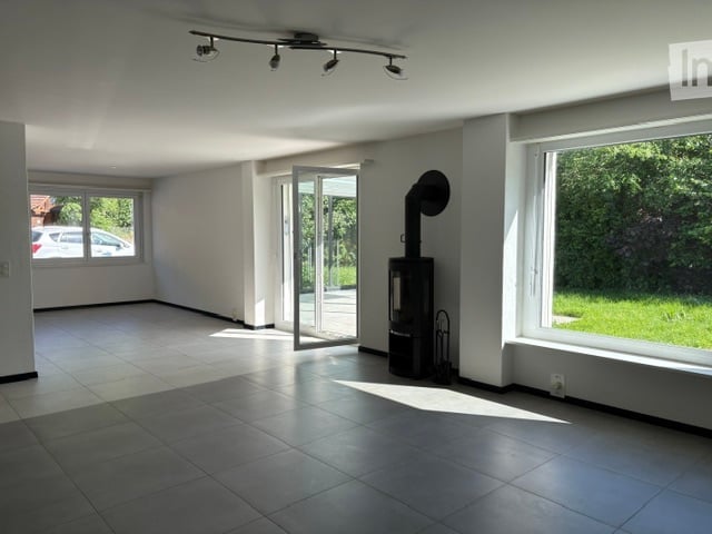 Empty room with white walls, tiled floor, large windows, and a sliding glass door leading to an outdoor area. No furniture or equipment is present.