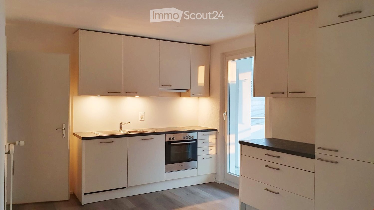Modern kitchen with white cabinets, a sink, an oven, and a window letting in natural light.