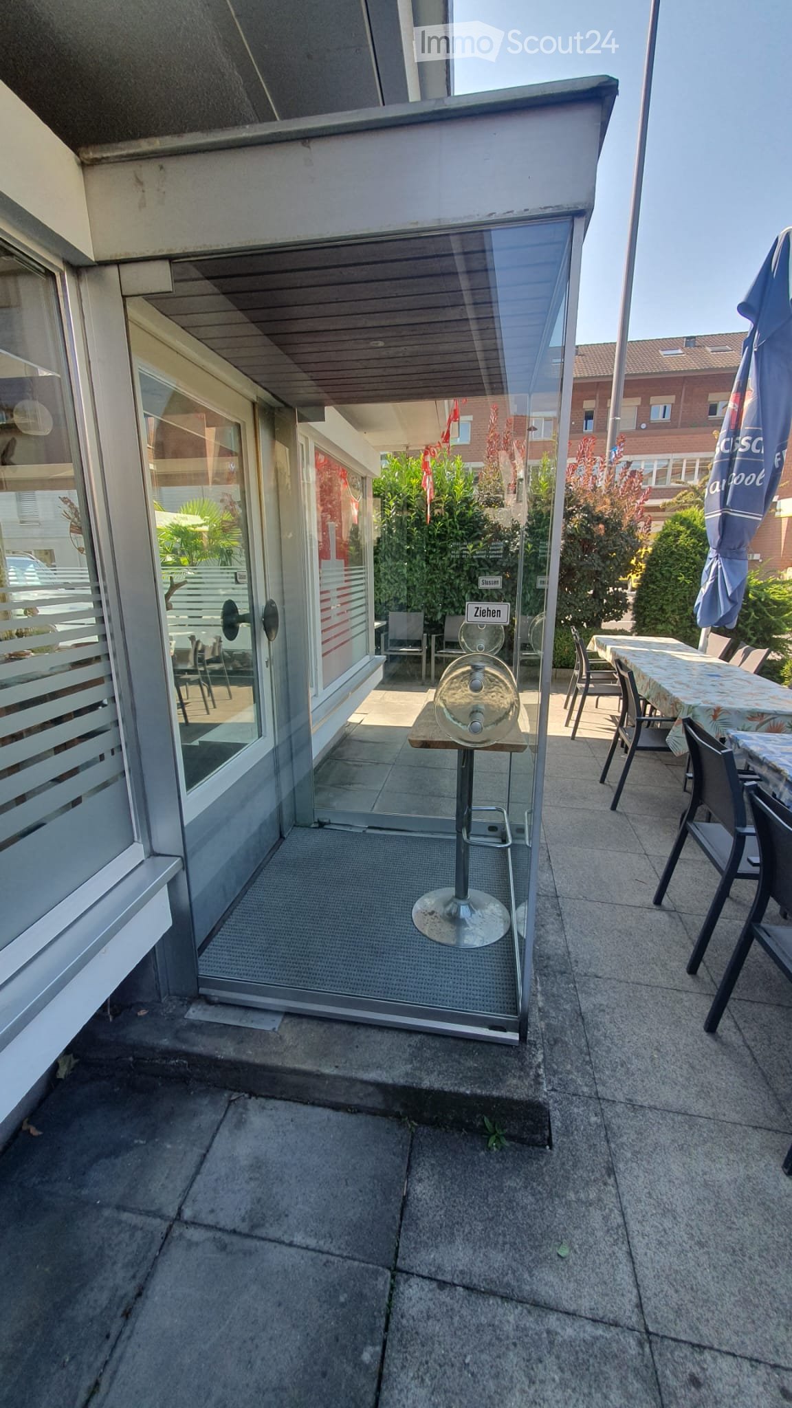 Balcony with a glass door leading to an indoor area, featuring a small table, chairs, and a stool.