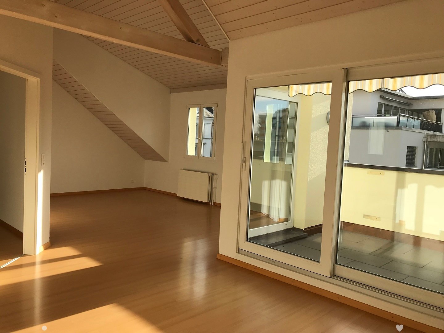 Empty room with wooden flooring, large windows, and a slanted wooden ceiling. No furniture or equipment present.