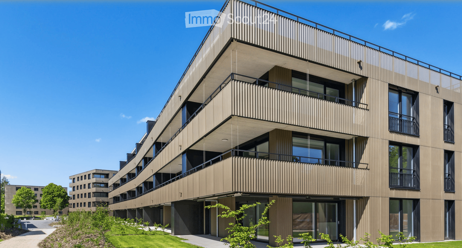 Modern multi-story building with a sleek, contemporary design featuring large windows, balconies, and a textured facade.
