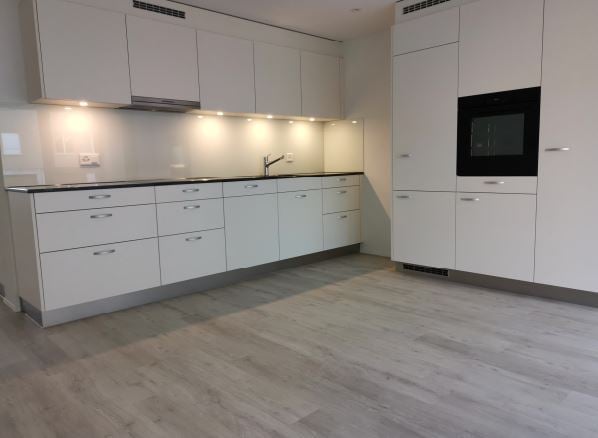 Modern kitchen with white cabinets, a sink, and an oven. The floor is made of light wood.