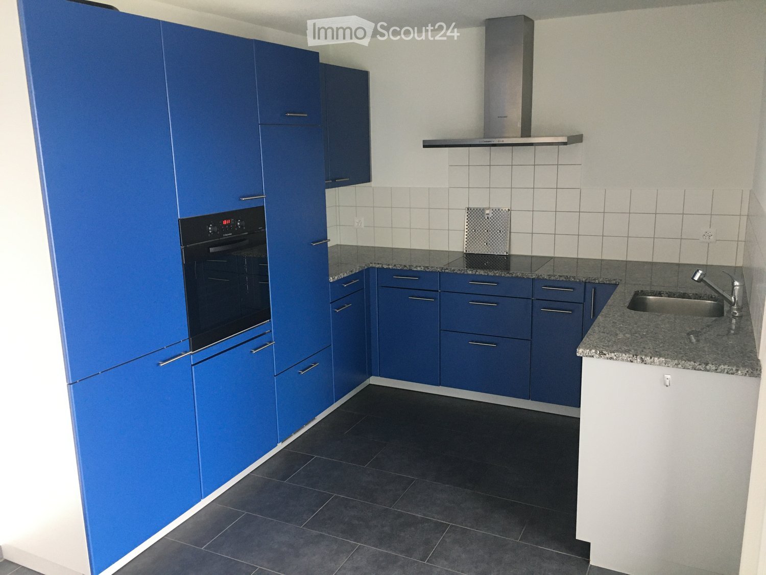 Modern kitchen with blue cabinets, black tiled floor, granite countertop, sink with faucet, black built-in oven and stove.