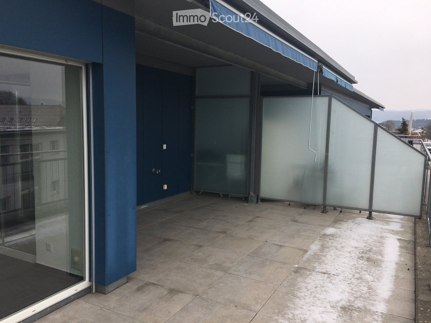 Balcony with tiled floor, glass partitions, and a blue awning on the roof.