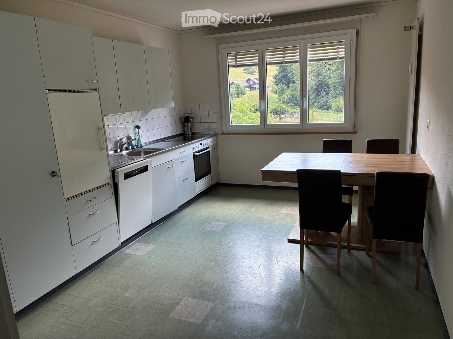 Modern kitchen with white cabinets, stainless steel sink, oven, dishwasher, and a wooden dining table with four chairs.