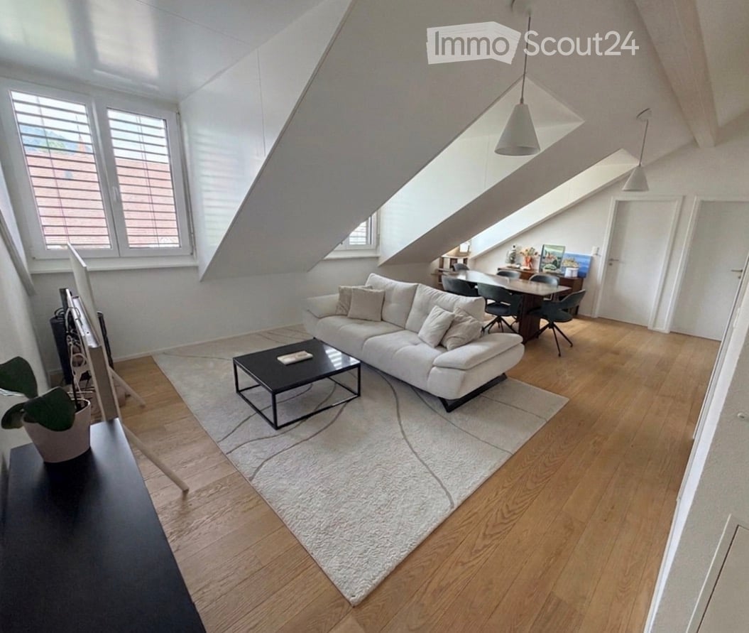 Modern living room with white sofa, black coffee table, dining area with table and chairs, pendant lights, and large windows with blinds.