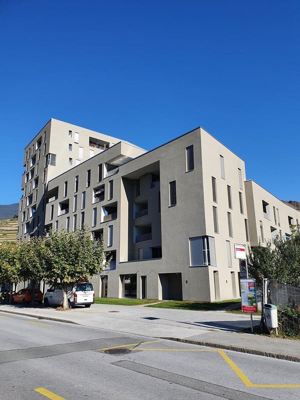 Modern multi-story residential building with a clean, contemporary design, featuring balconies and large windows.