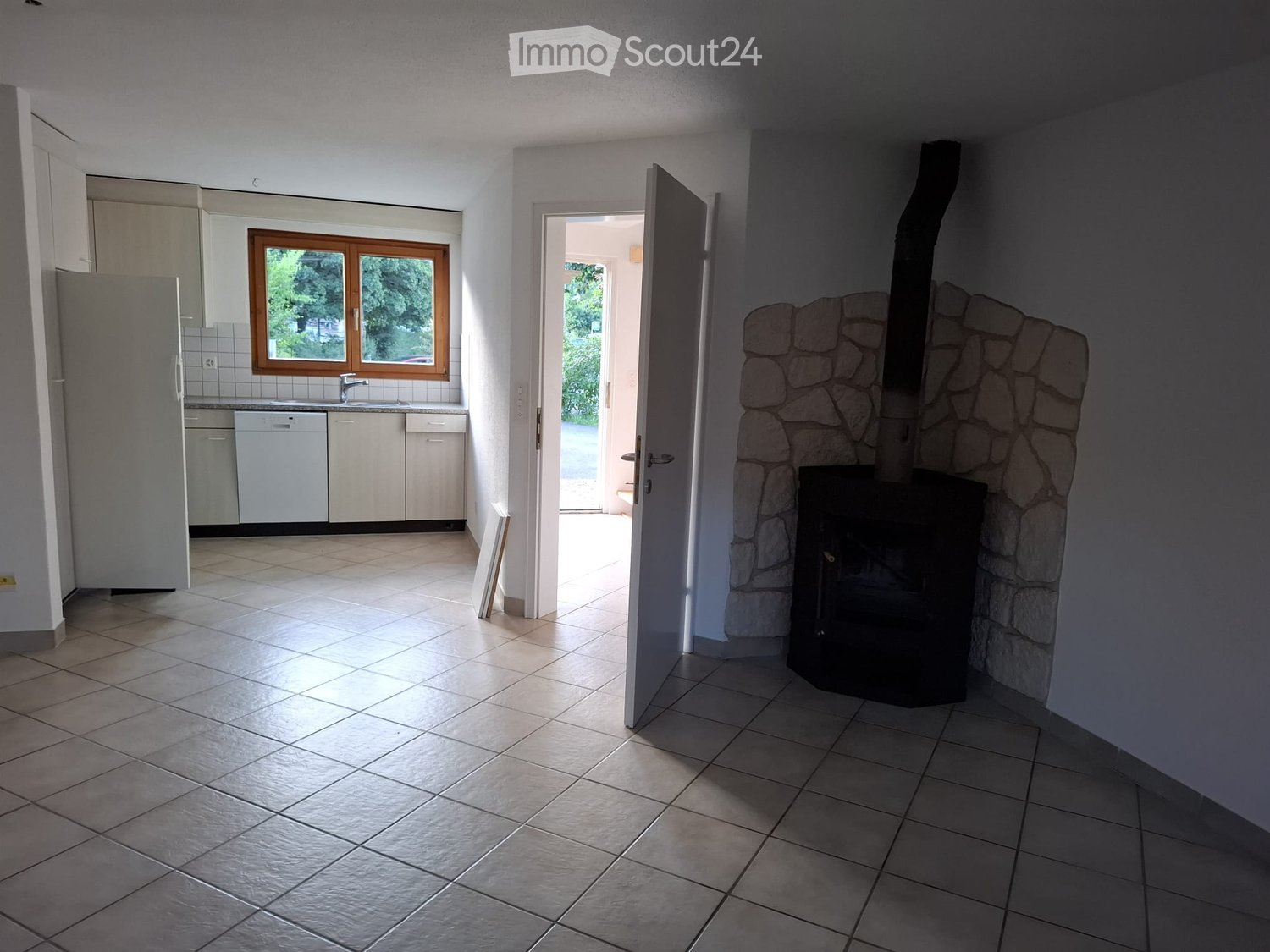 Bright room with tiled floor, fireplace, and an open doorway leading to another room with a window and kitchen area.