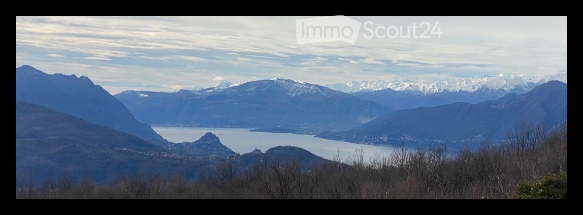 Panoramic view of a lake surrounded by snow-capped mountains and a town in the distance.