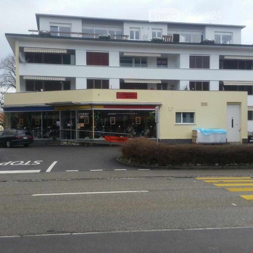 Two-story building with a bike shop storefront, multiple windows, awnings, and a small balcony area on the roof.