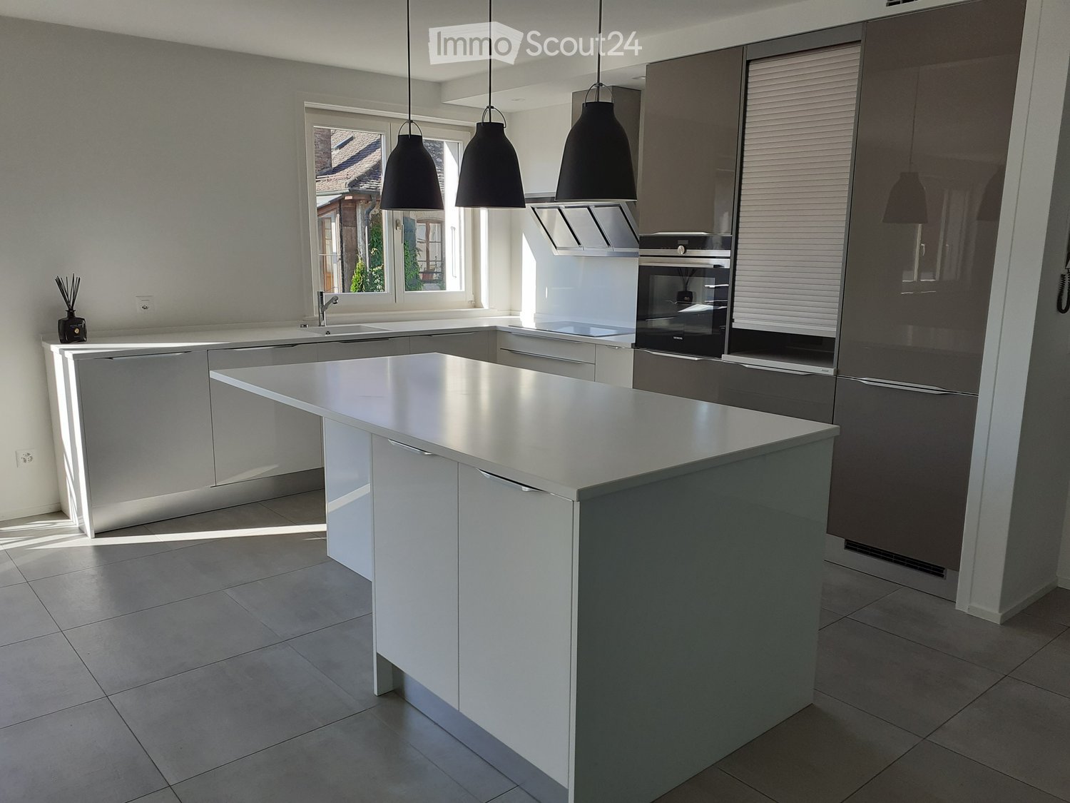 Modern kitchen with white cabinets, stainless steel island, sink, oven, refrigerator, and pendant lights.