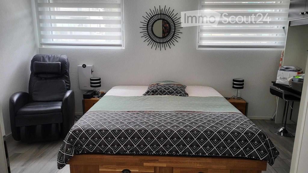 Cozy bedroom with a double bed, patterned duvet, nightstands with lamps, a black leather chair, and a decorative mirror on the wall.