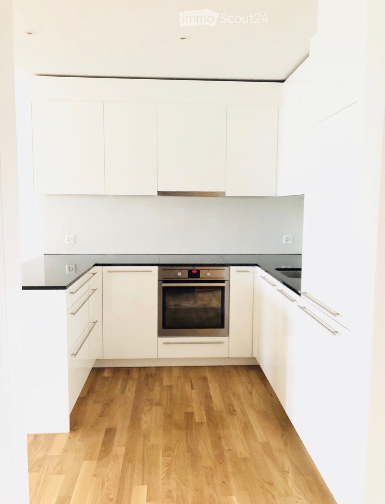 Modern kitchen with white cabinets, wooden flooring, and a built-in oven.