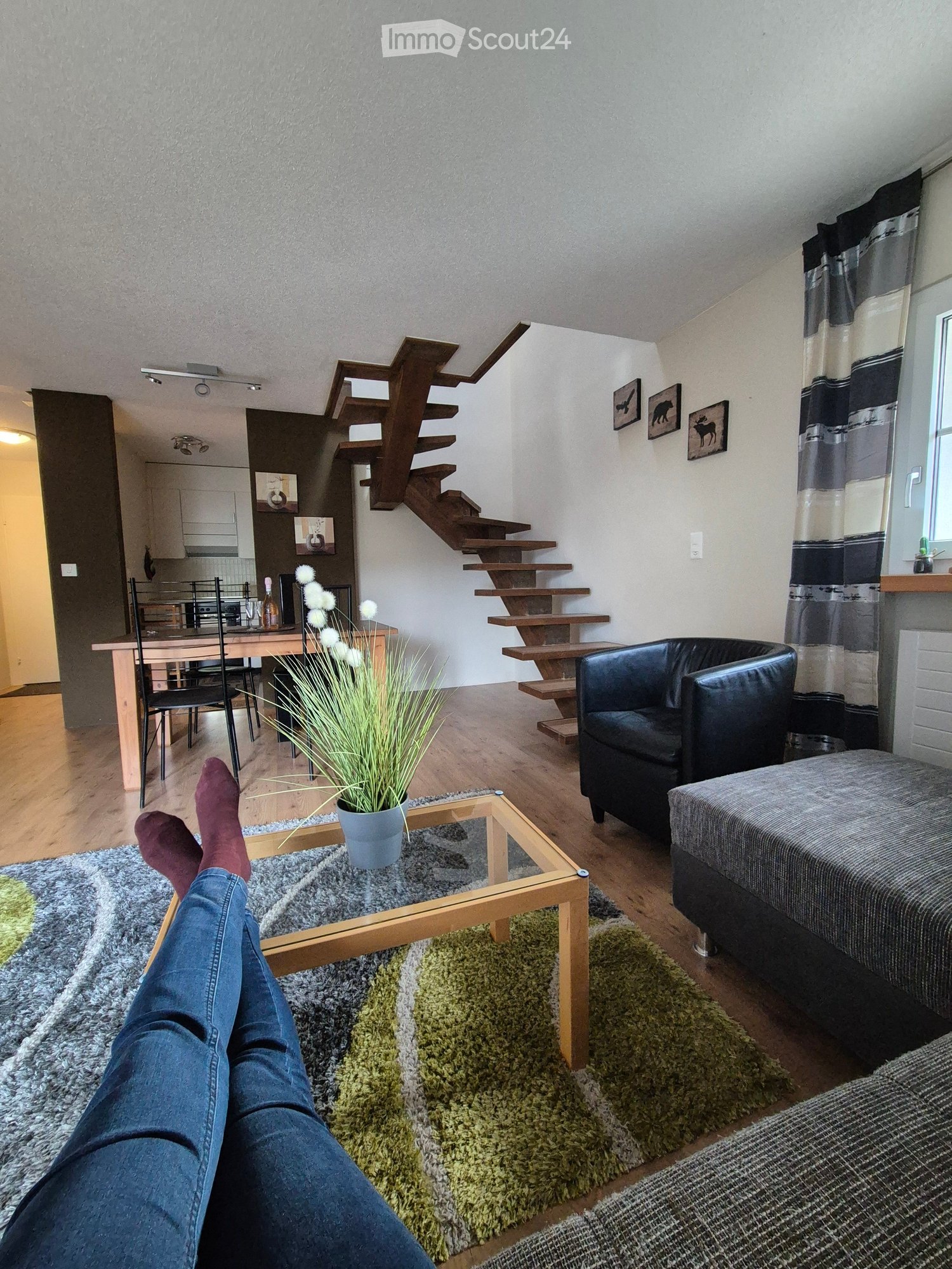 Living room with a sofa, coffee table, dining table, chairs, and a staircase leading to an upper level.